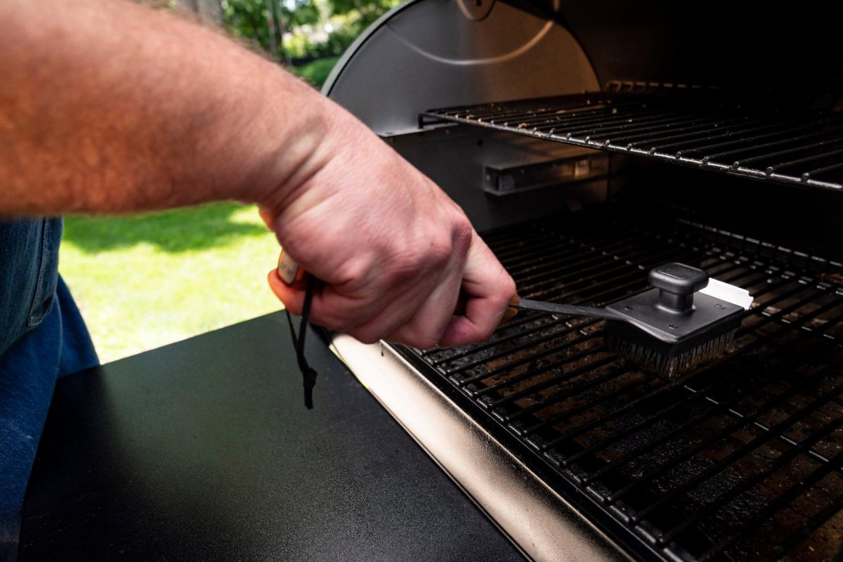 Homeowner cleaning the grease tray and grill grates of a Traeger pellet grill in a Binghamton NY backyard
