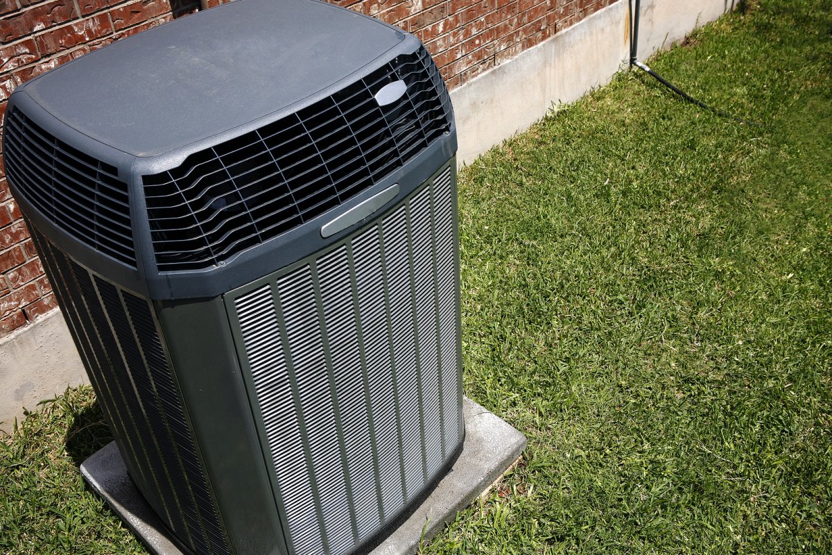 HVAC technician repairing a central air conditioner condenser unit outside a Binghamton NY home in summer