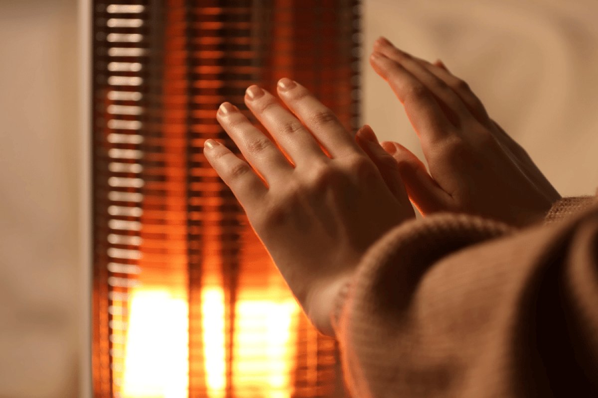 Woman with her hands placed in front of a space heater trying to stay warm after her furnace broke down