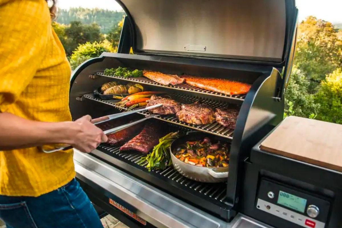 Traeger pellet grill with smoke rising and a brisket, wings, and corn cooking on multiple grate tiers during a Memorial Day backyard cookout in the Southern Tier