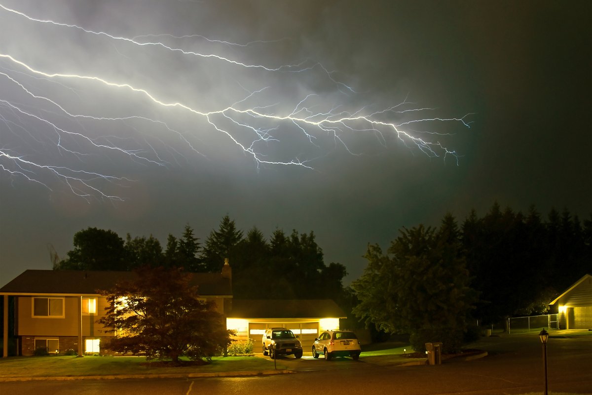 Lightning illuminating the sky above a Binghamton area home with a central air conditioning condenser unit visible in the yard during a summer thunderstorm