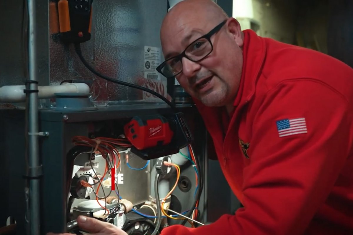 NATE-certified HVAC technician inspecting and servicing an outdoor central air conditioner condenser unit at a Binghamton area home during a spring tune-up visit